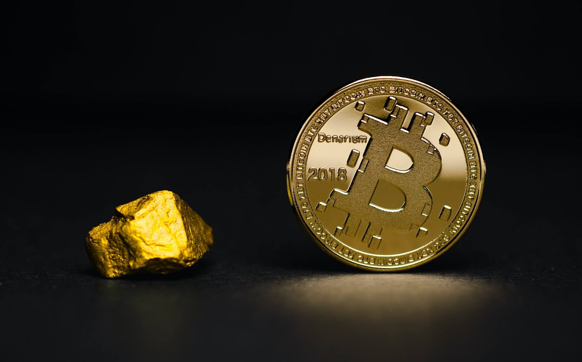 A gold Bitcoin coin stands upright beside a small gold nugget, perfect for your website’s striking visuals.