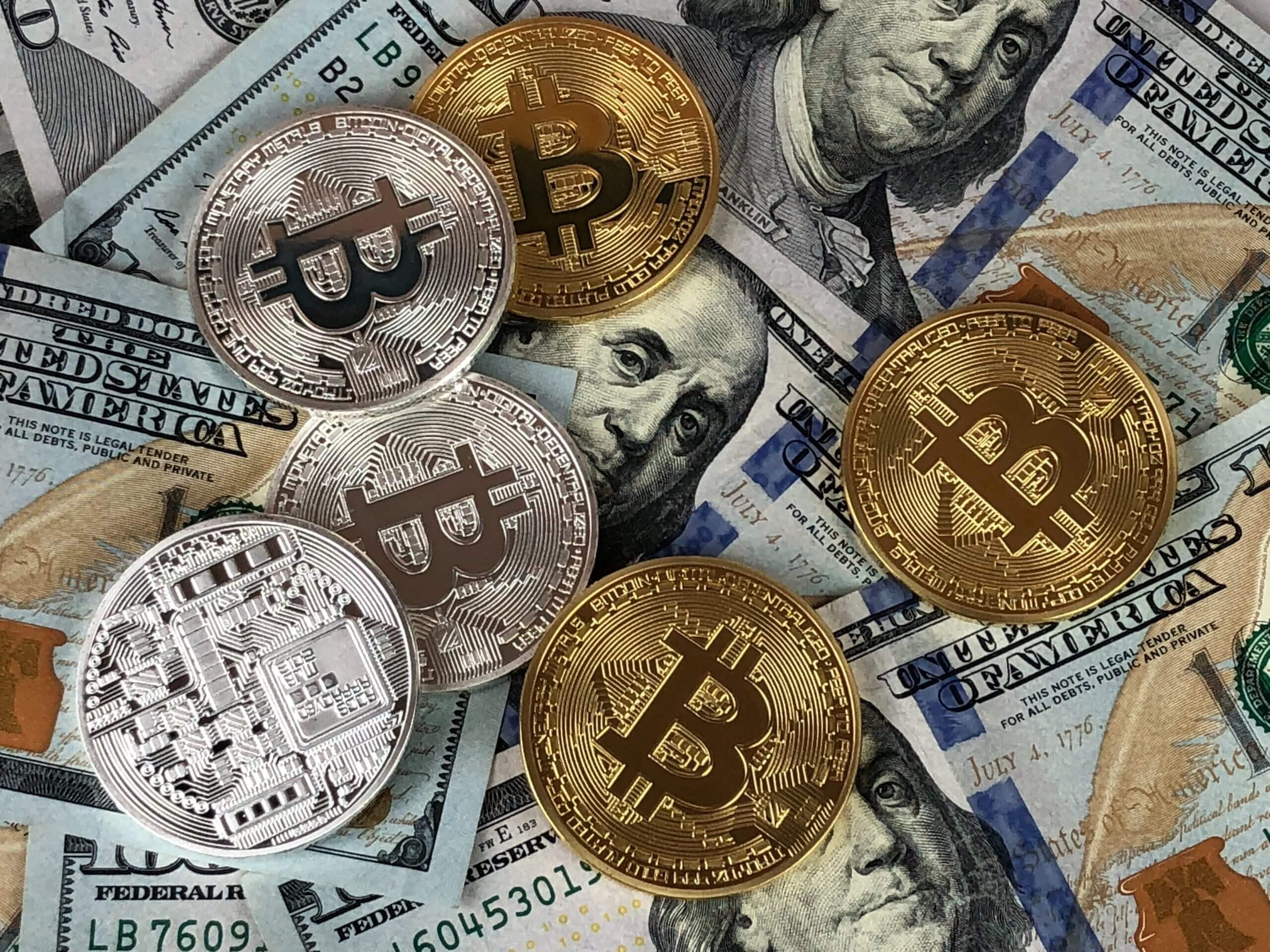 Stacks of silver and gold Bitcoin tokens on U.S. hundred-dollar bills, perfect for your website’s finance visuals.