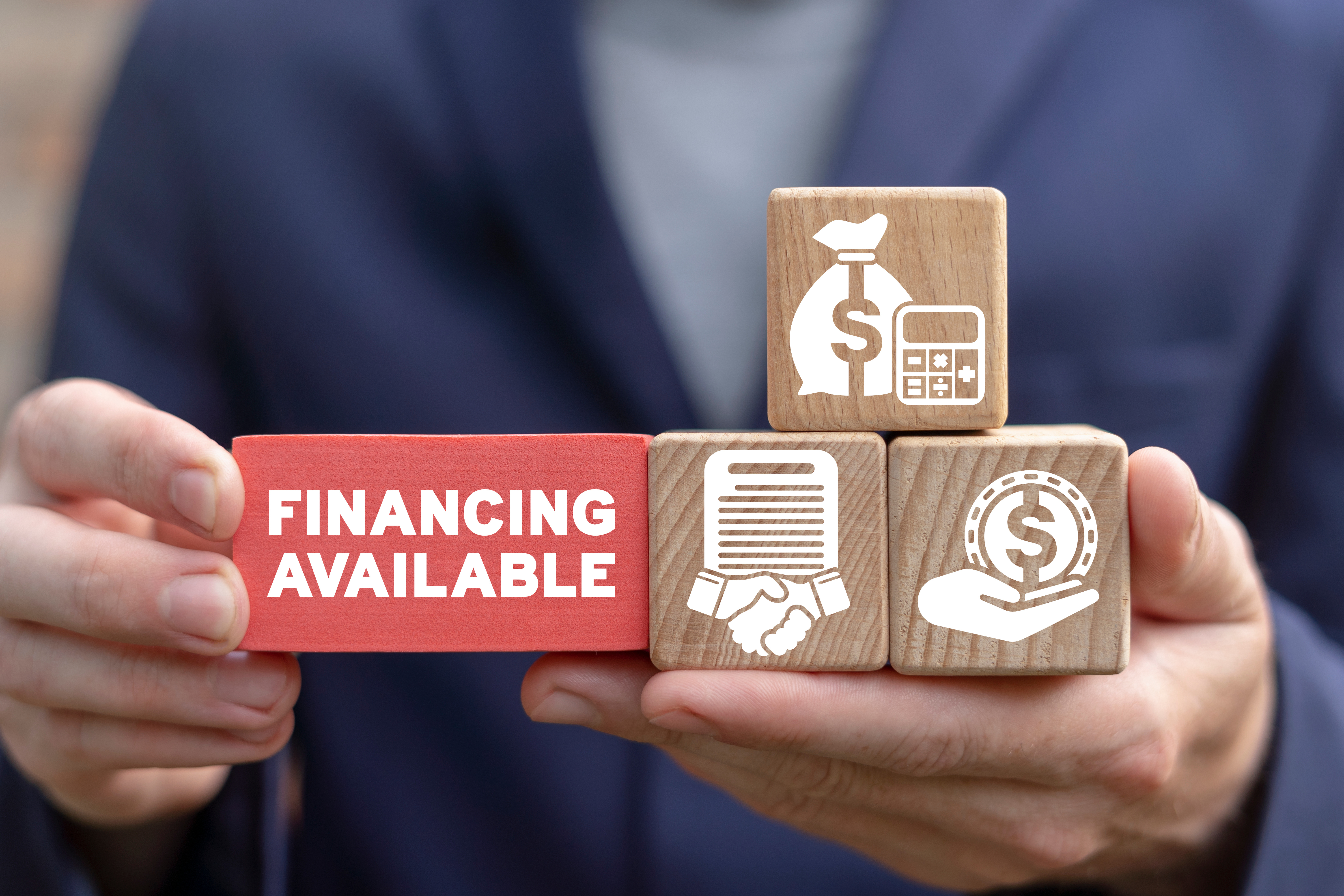 A person holds wooden blocks with finance icons and a red block labeled Financing Available.