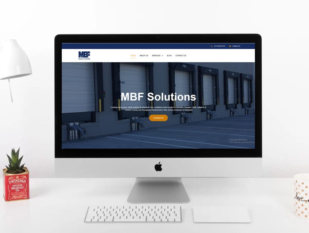 A computer monitor displays the MBF Solutions website with a warehouse image and navigation menu.