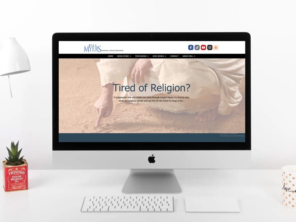 A desktop computer displays a website with the headline Tired of Religion? over an image of a person drawing in sand.