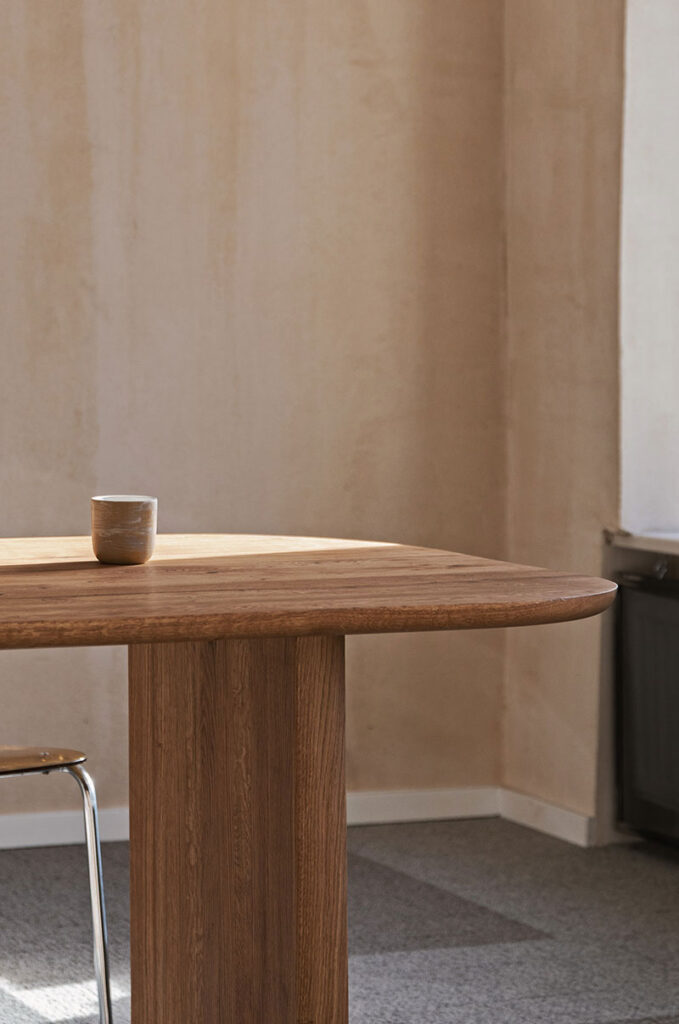 A ceramic cup sits on a wooden table in a minimal, softly lit room with neutral walls and carpeted floor.