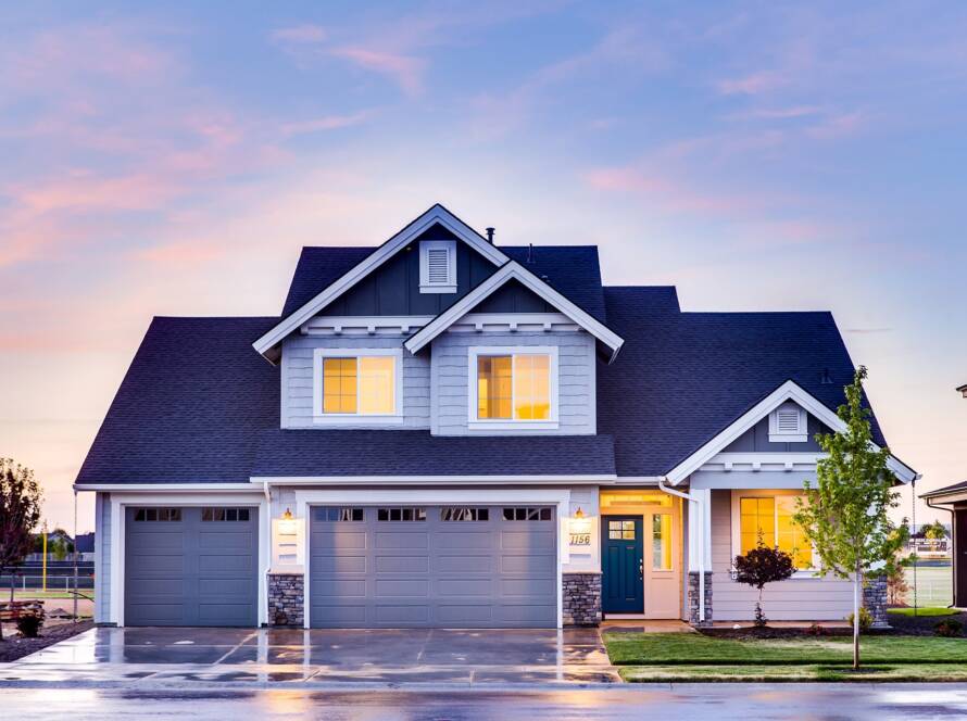 Modern two-story house with three garages, illuminated windows at sunset, and a tree in the front yard for your website.