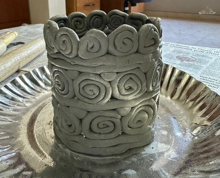 A handmade clay pot with spiral coil designs sits on a metal tray, perfect for featuring on your website.