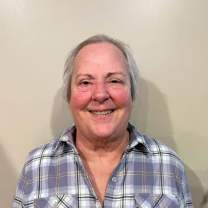 Smiling older woman with short gray hair in plaid shirt, perfect for a website about seniors against a beige background.