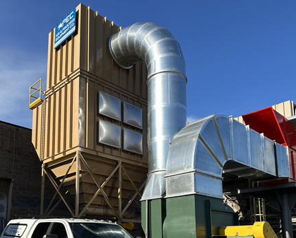 Large industrial dust collection system with metal ductwork and a tan storage unit under a blue sky.
