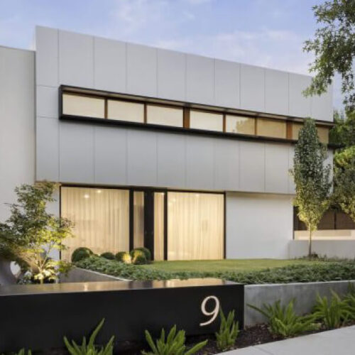 Modern two-story house with large windows, wooden door, manicured lawn, and website-inspired minimalist landscaping.